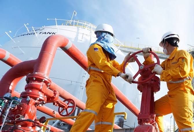 Two operators in coveralls performing valve operations at a storage tank
